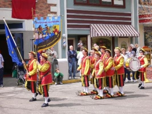 Vaandeldragers en loopsteltenlopers op lange planken in een optocht