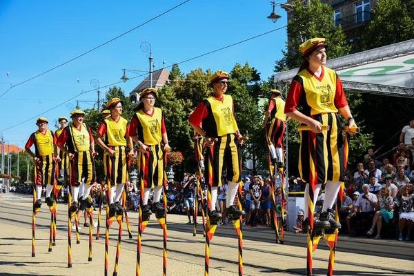 Steltenlopers in gele hesjes op een zonnig plein vol publiek