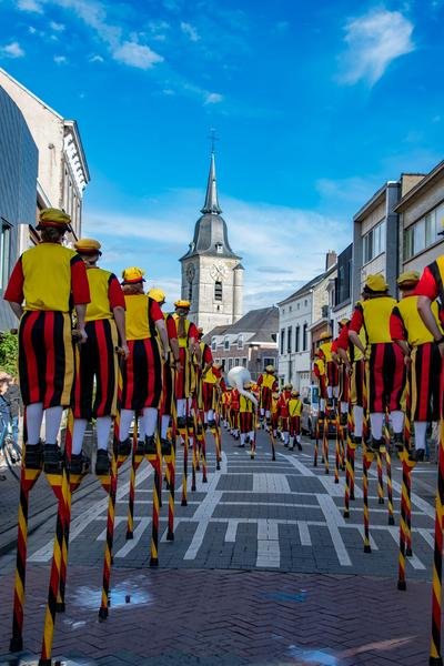 Stoet steltenlopers in een straat met een kerktoren op de achtergrond