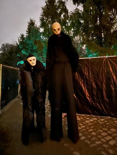 Twee gemaskerde figuren in het zwart, één op stelten