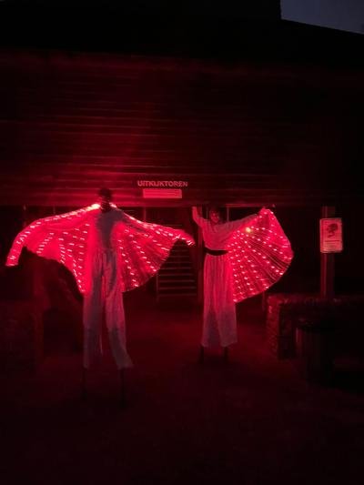 Twee steltenlopers met rode lichtvleugels voor een gebouw